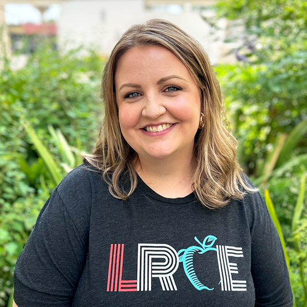 LRCE-Headshot---Addie-Kelley-Square Addie Kelley, smiling and wearing a black LRCE shirt, standing in front of a green garden background.