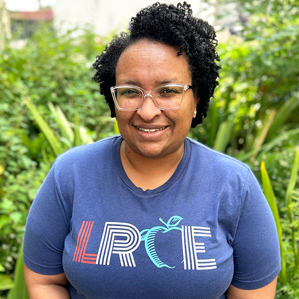 LRCE-Headshot---Juanique-Dugas-Square Juanique Dugas, smiling and wearing a black LRCE shirt, standing in front of a green garden background.