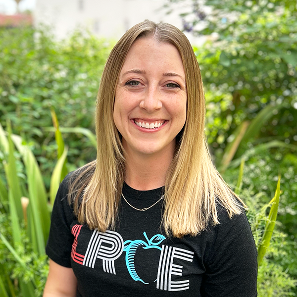 LRCE-Headshot---Katie-Hagan-Square Katie Hagan, smiling and wearing a black LRCE shirt, standing in front of a green garden background.