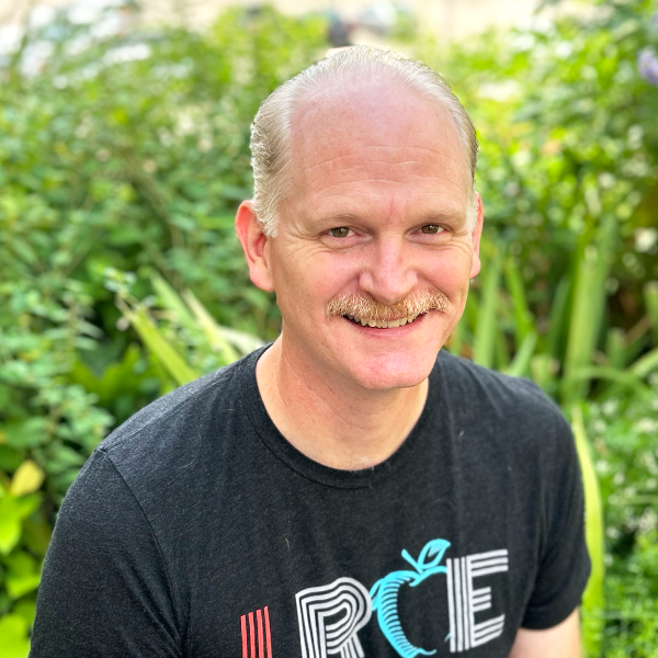 LRCE-Headshot---Kyle-Finke-Square Kyle Finke, smiling and wearing a black LRCE shirt, standing in front of a green garden background.
