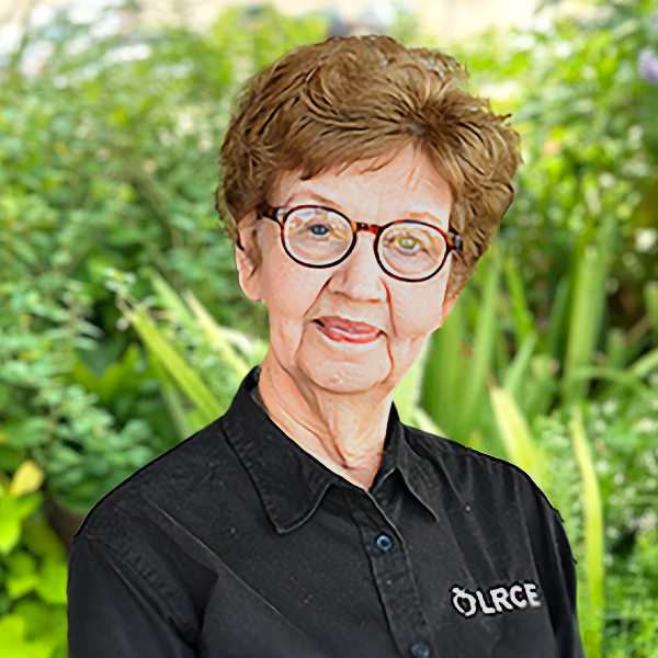 LRCE-Headshot---Veronica-Stanek-Square Veronica Stanek, smiling and wearing a black LRCE shirt, standing in front of a green garden background.