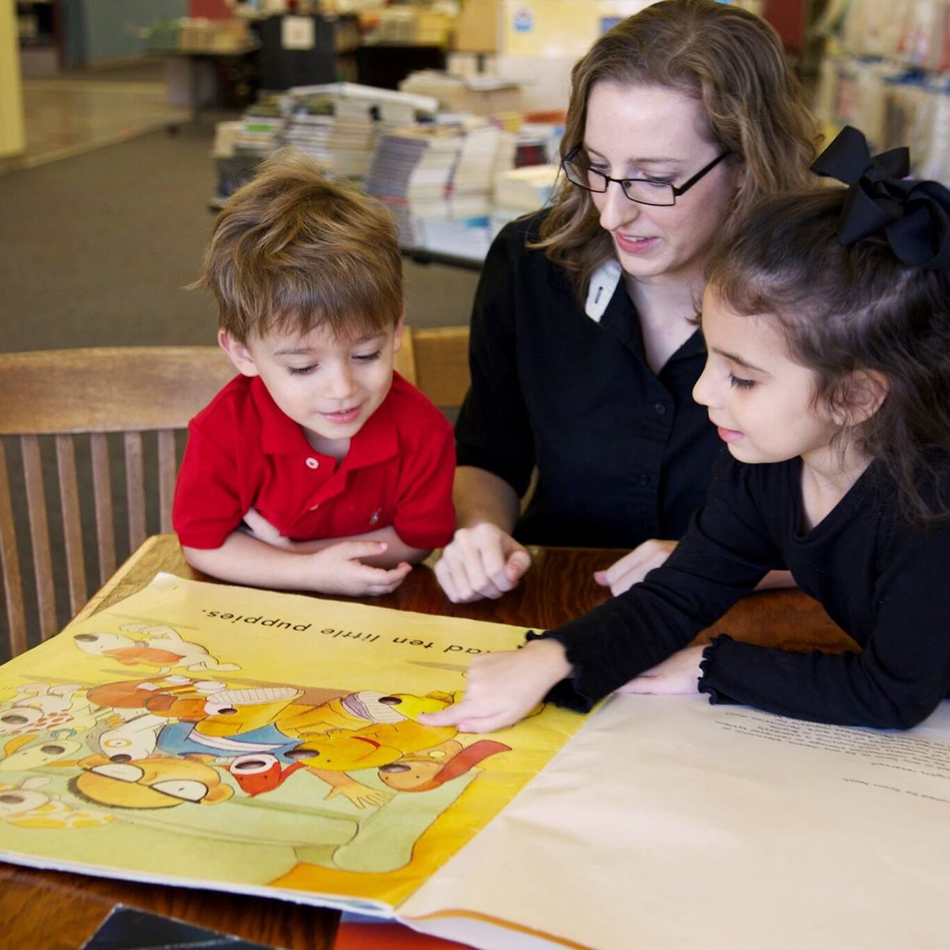 A teacher reads a large illustrated book to two young children in a classroom setting, promoting early childhood education and literacy support at LRCE.