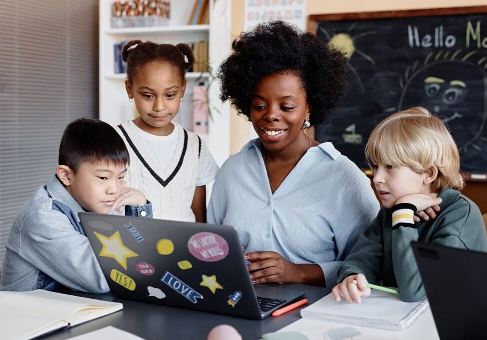 “Teacher and diverse group of students working together on a laptop in the classroom, highlighting LRCE’s commitment to inclusive and collaborative learning environments.