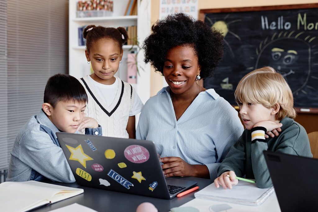 “Teacher and diverse group of students working together on a laptop in the classroom, highlighting LRCE’s commitment to inclusive and collaborative learning environments.